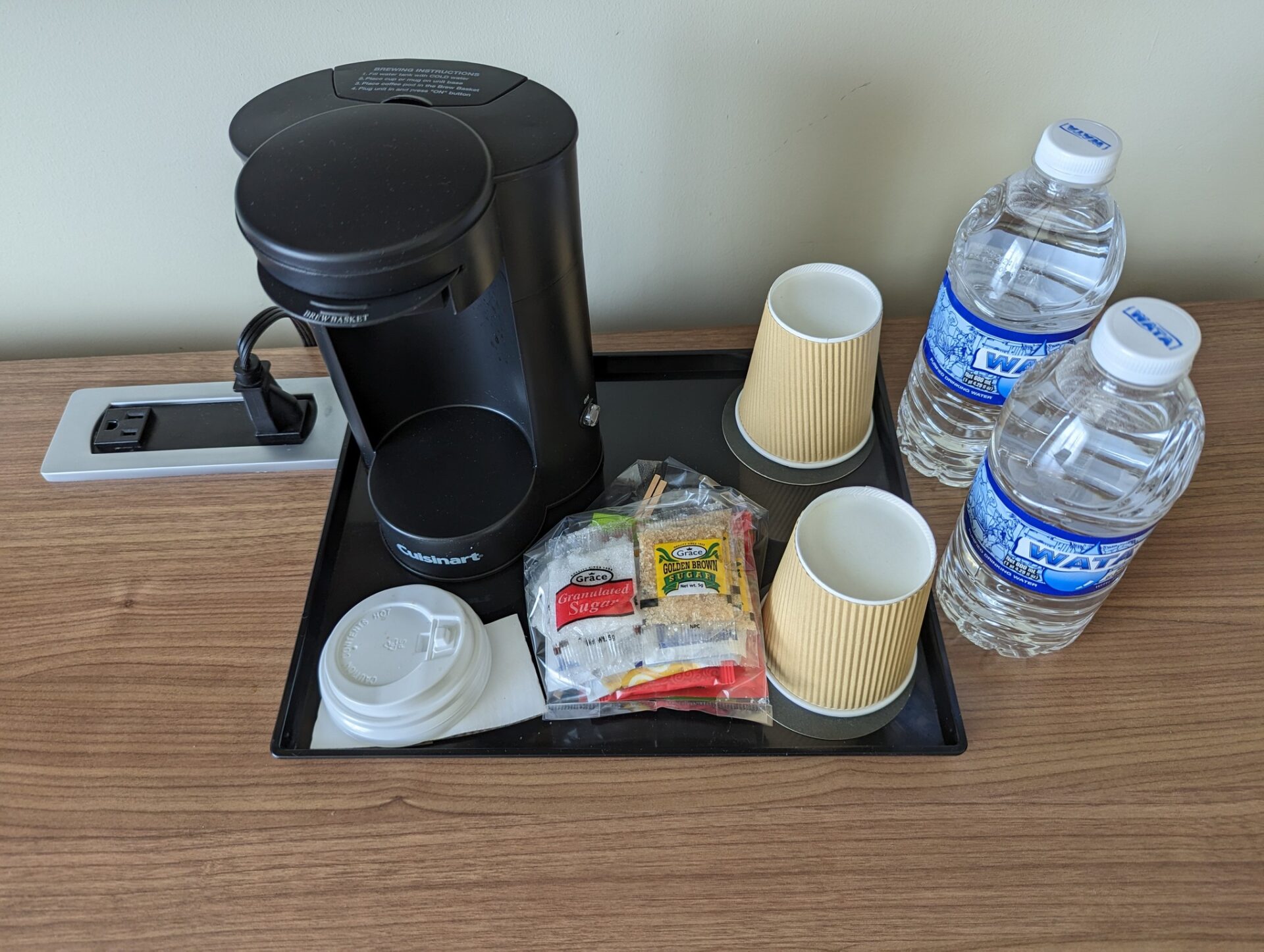 a tray with coffee maker and cups and water bottles on a table