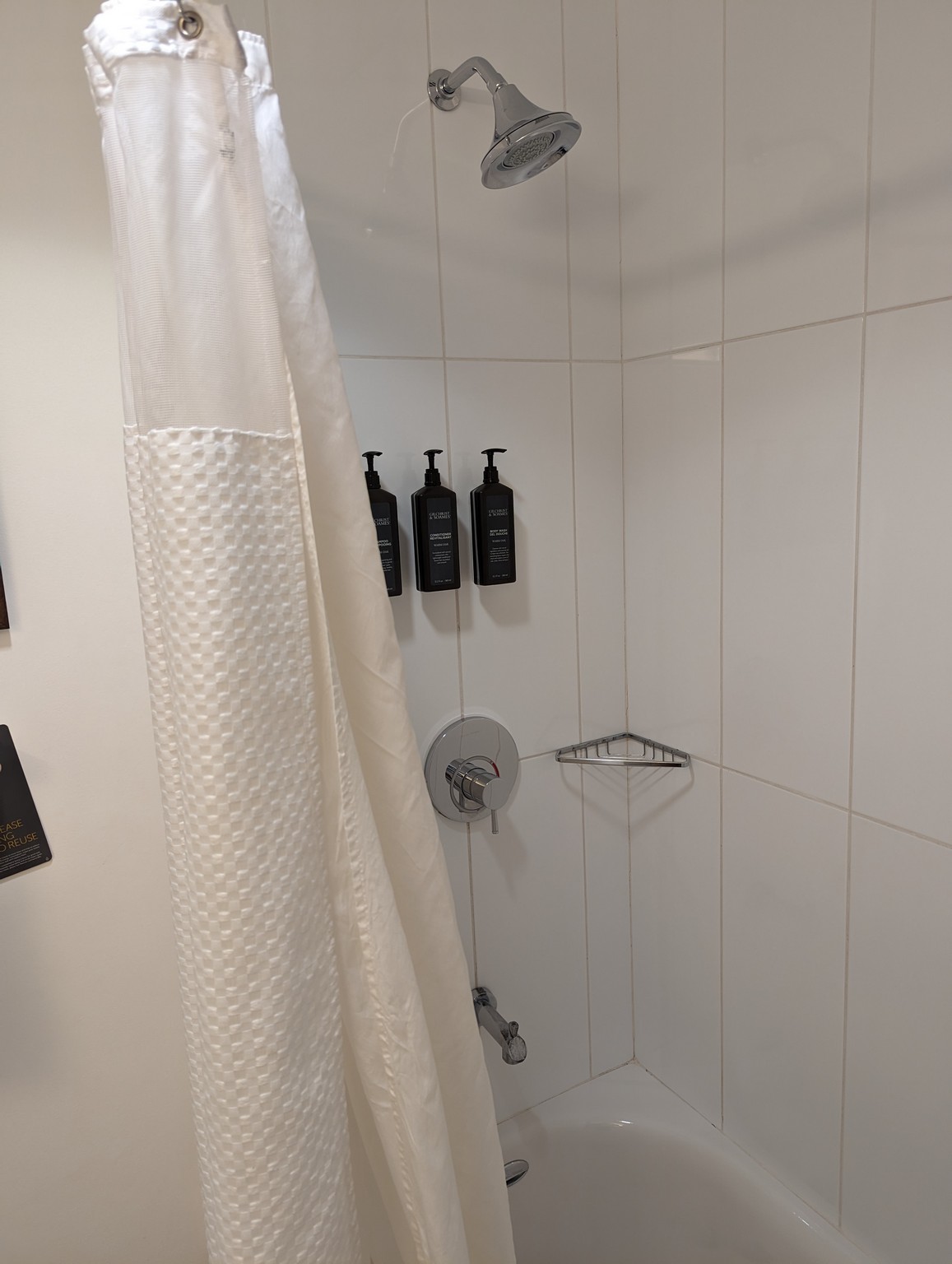 a shower with a white curtain and black bottles