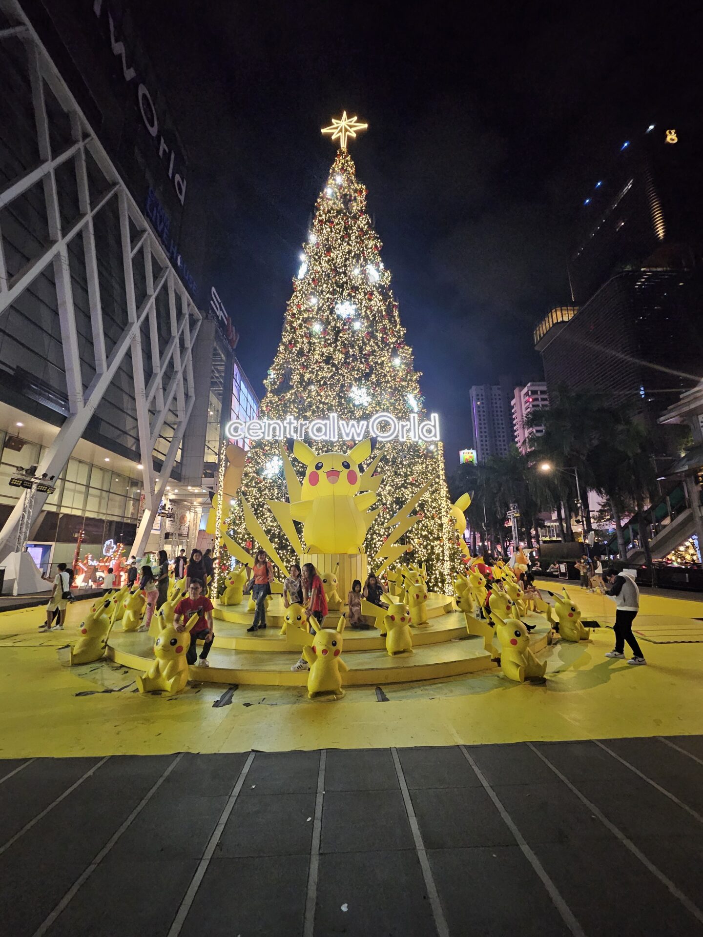 a large christmas tree with a large yellow tree and people around it