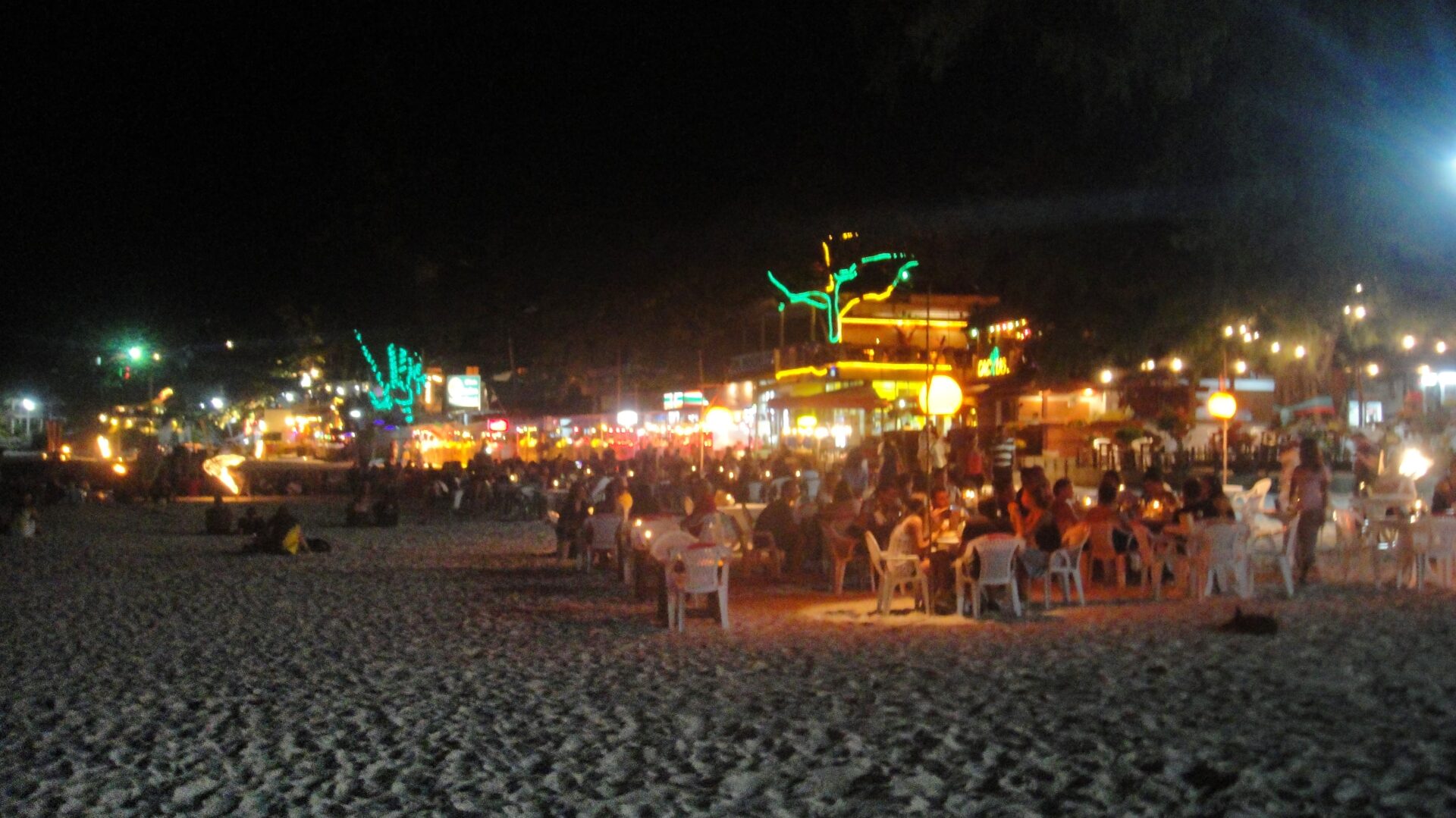 a group of people sitting at tables on a beach at night