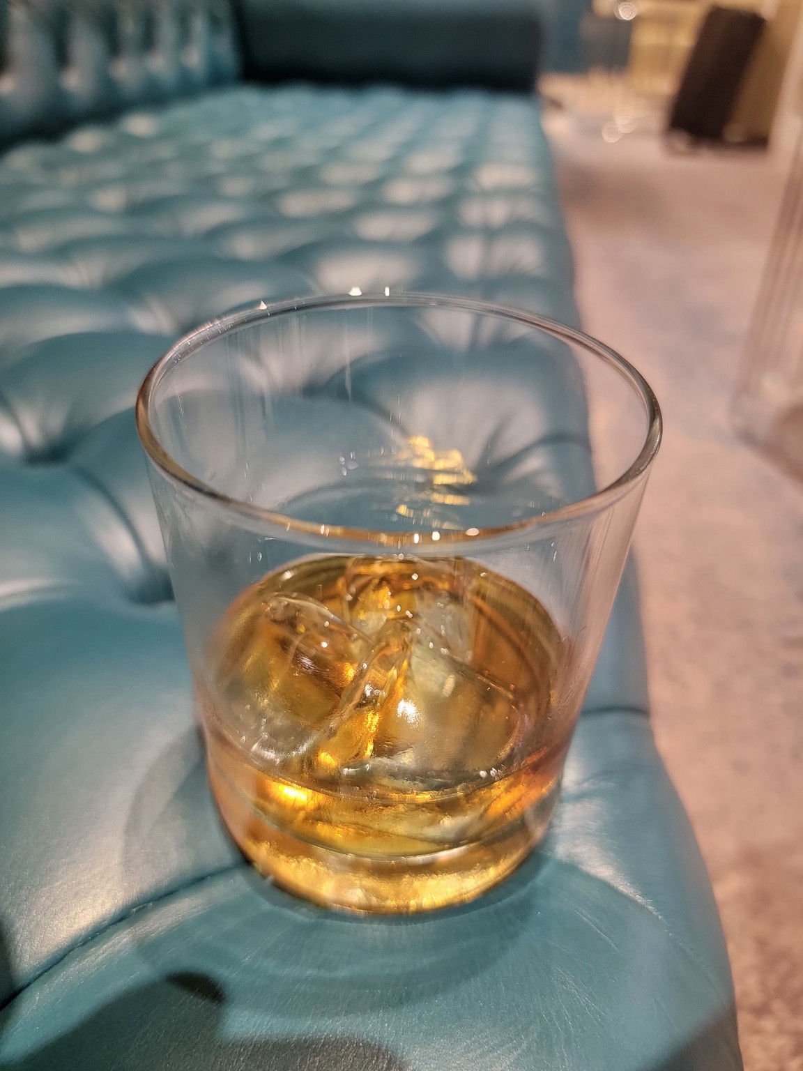 a glass of alcohol with ice on a blue leather couch