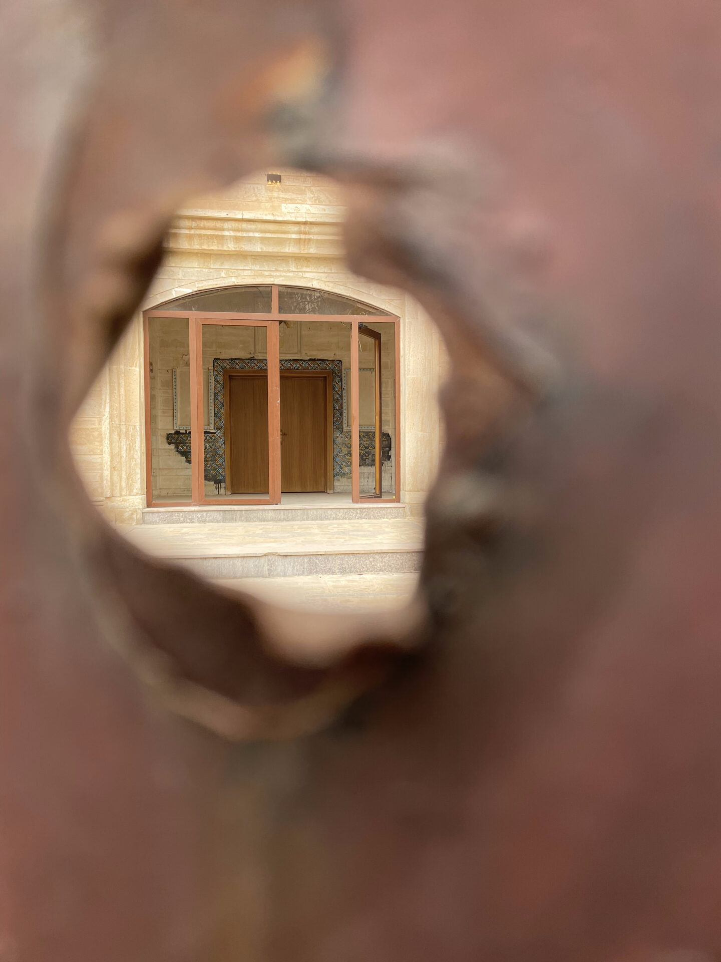 a hole in a metal wall with a door and a building