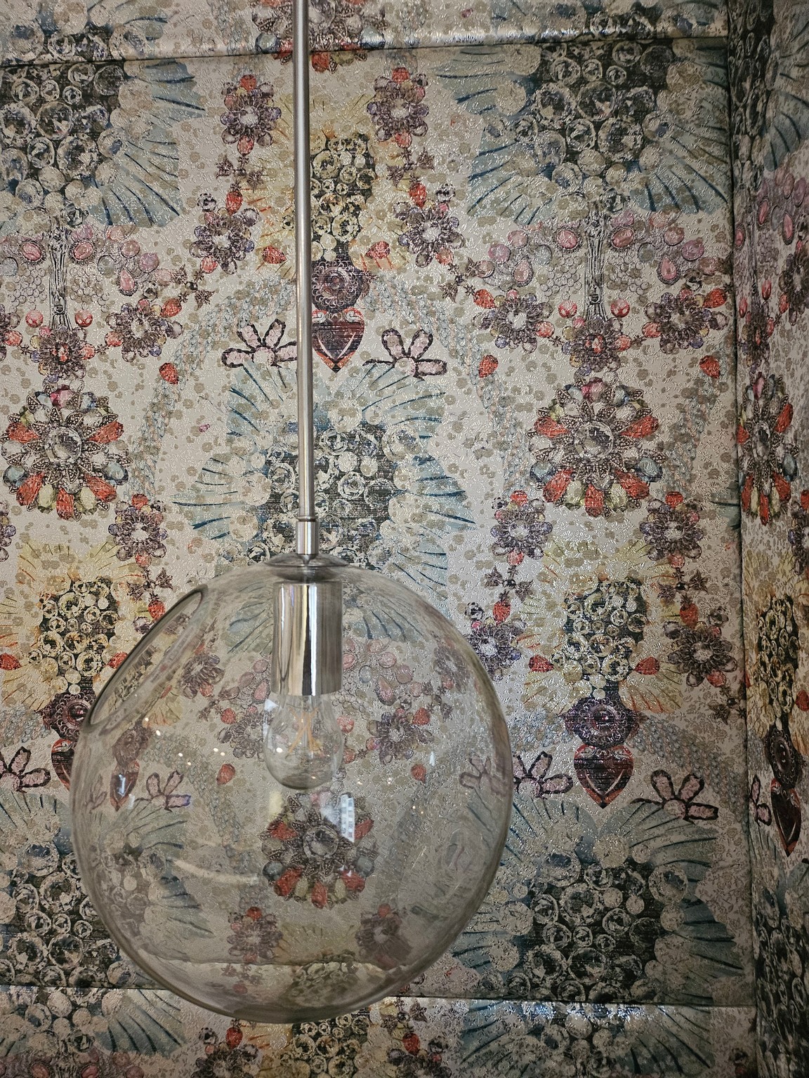 a glass light fixture in front of a floral wallpaper