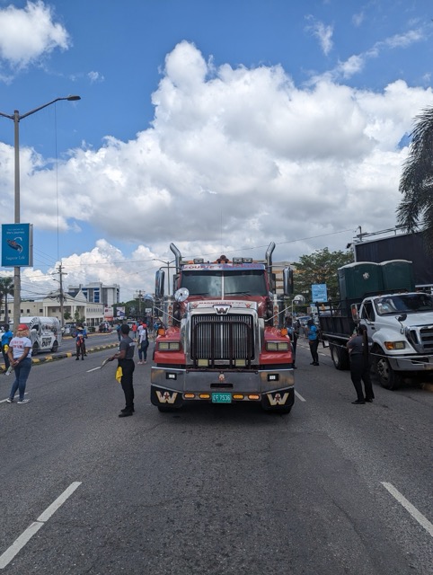 a red truck on a road with people standing around